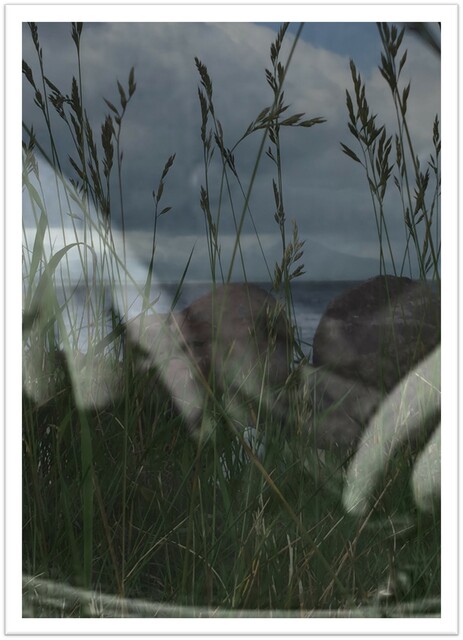 A pair of transparent hands manipulate what appears to be cloth in an image superimposed over a photograph of tall grass and large boulders on an Irish coastline. 